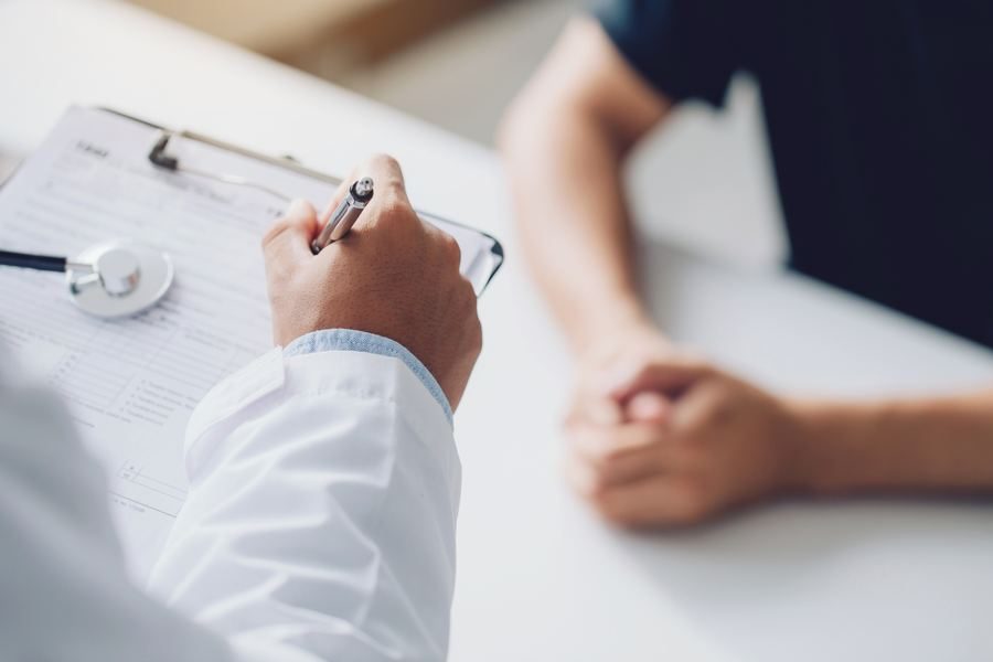A clinician with a clipboard beside a patient's hands