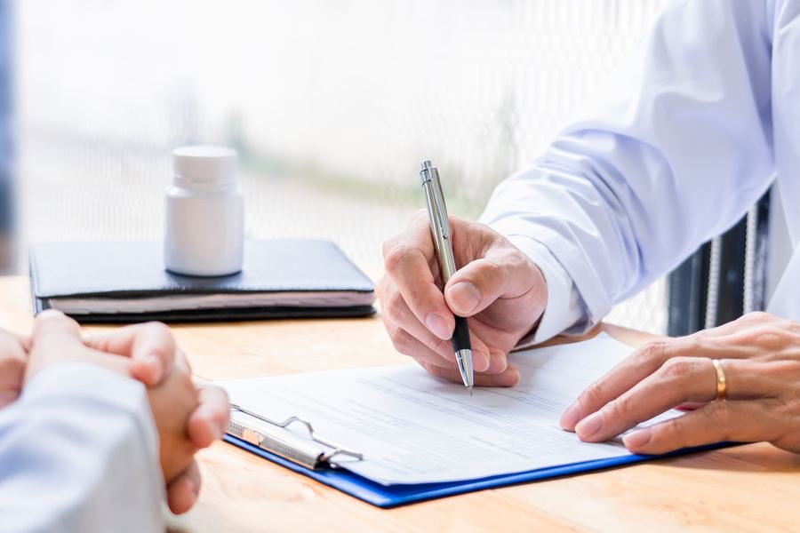 Signing a referral form beside a bottle of tablets